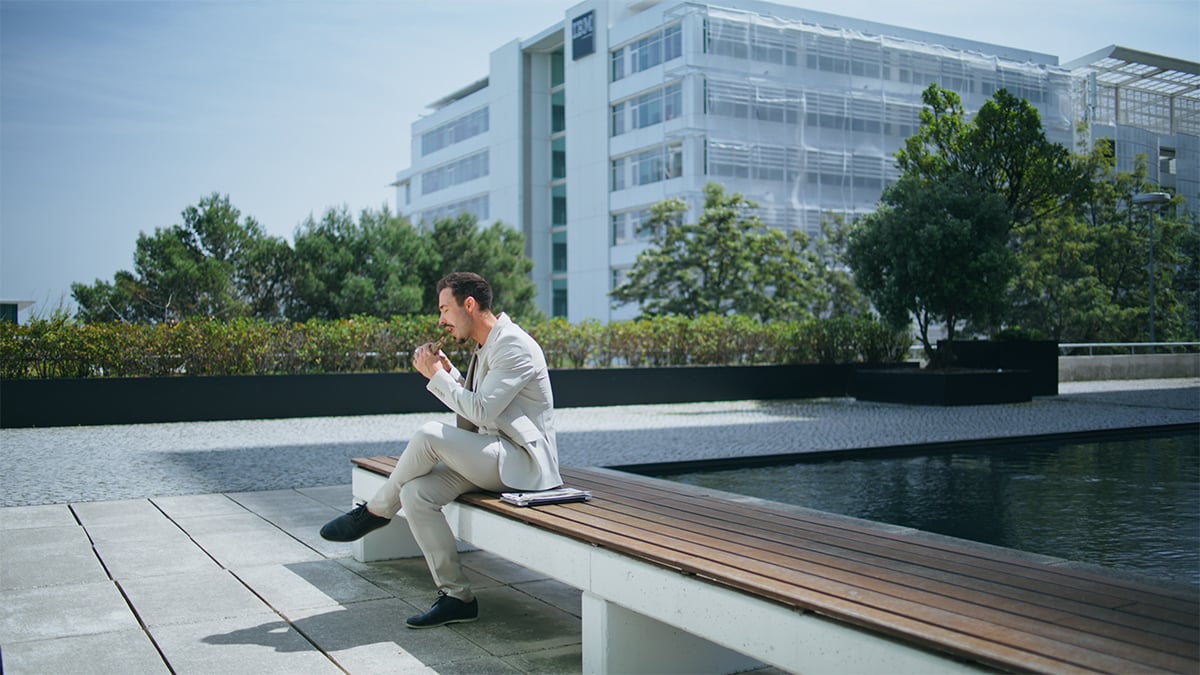 man in suit sitting on a bench outside taking a break and eating